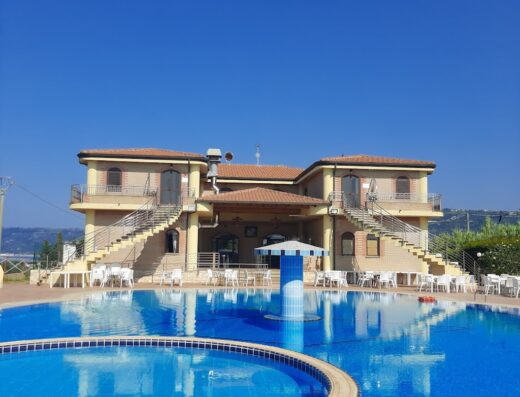 Hotel Granduca vista piscina esterna con edificio a due piani, sedie e tavoli bianchi per relax e ristoro, cielo azzurro terso.