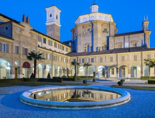 Hotel I Somaschi: vista del cortile interno con fontana circolare, portici ad arco, giardini curati e l'imponente architettura dell'edificio storico.
