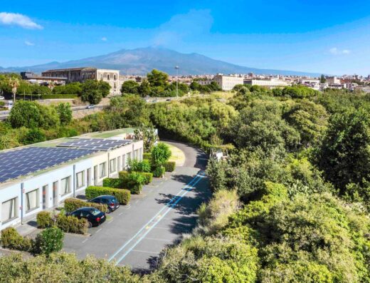 Vista dell'Hotel ibis Styles Catania Acireale con parcheggio, pannelli solari sul tetto e l'Etna sullo sfondo