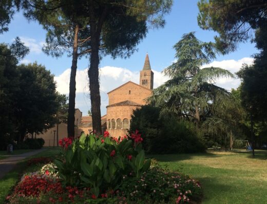 Vista suggestiva di un'antica chiesa con campanile, circondata da alberi rigogliosi e aiuole fiorite, Hotel Italia