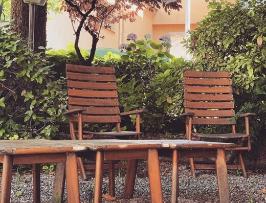 Area relax all'aperto dell'Hotel Italia con tavolo e sedie di legno in giardino, ideale per un soggiorno rilassante e confortevole.