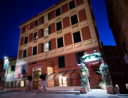 Hotel La Camogliese exterior at night, featuring a multi-story building with red and white facade, dark green shutters, and illuminated sign.