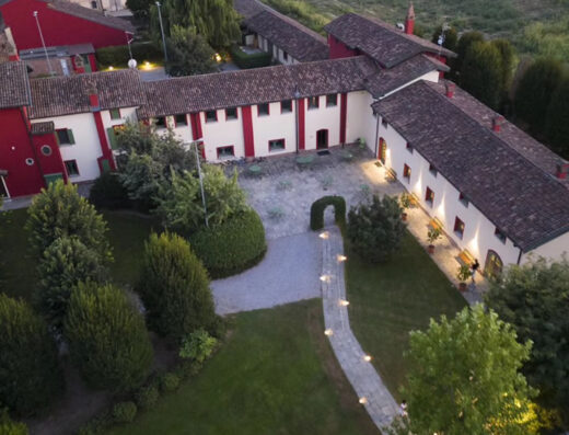 Aerial view of Hotel La Corte San Lorenzo, featuring the building's red and white facade, tiled roof, courtyard, and surrounding green lawns with a stone path.