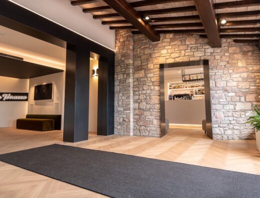 Interno dell'Hotel La Terrazza con pavimento in legno a spina di pesce, pareti in pietra, bar sullo sfondo e tappeto grigio.
