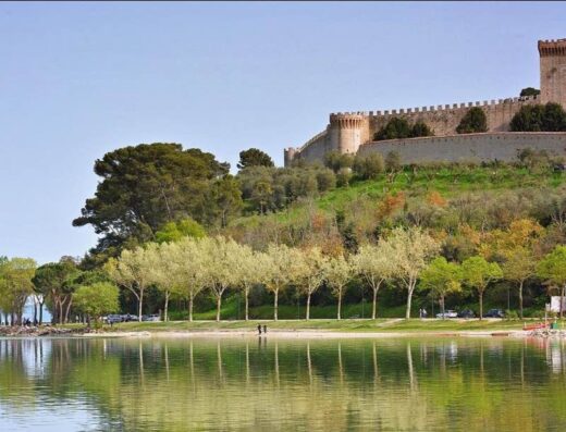 Hotel La Torre vista lago, con la rocca medievale sullo sfondo e alberi che si riflettono nell'acqua.