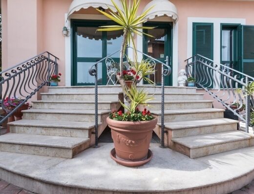 Ingresso dell'Hotel La Villetta con scalinata in pietra, ringhiere in ferro battuto, piante ornamentali in vaso e tende parasole.