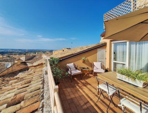 Terrazza panoramica dell'Hotel Lauri con tavolo, sedie, ombrellone e vista sulle colline marchigiane, ideale per un soggiorno rilassante e indimenticabile.