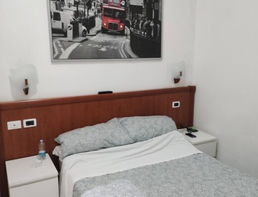 Camera dell'Hotel Les Artes con letto matrimoniale, comodini, lampade da parete e quadro di un autobus a due piani di Londra.
