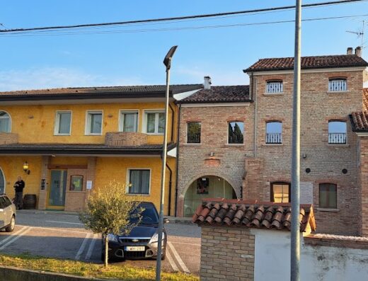Hotel Locanda Dolce Vita exterior view with yellow and brick buildings, cars parked in front, and clear sky.