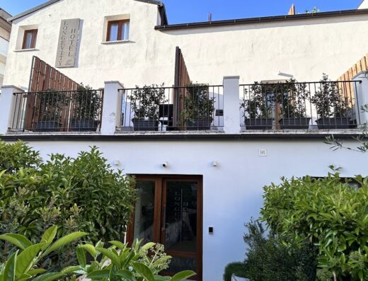 Esterno dell'Hotel Longevity a Tortolì, Sardegna, con balcone decorato con piante e ingresso visibile tra la vegetazione.