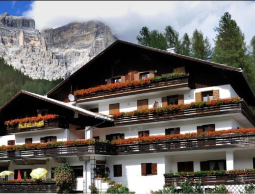Hotel Maè e Residence Panorama, un rifugio accogliente con balconi fioriti e vista mozzafiato sulle Dolomiti, ideale per viaggi e vacanze indimenticabili.