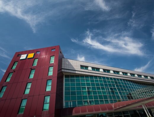 Vista esterna dell'Hotel Mastai nelle Marche, che mostra la sua architettura moderna e il cielo azzurro con nuvole bianche sullo sfondo.