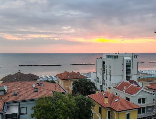 Vista panoramica dell'Hotel Mediterraneo sull'Adriatico al tramonto, con edifici colorati e spiaggia attrezzata.