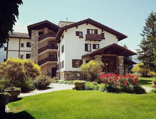 Hotel Milleluci: vista esterna dell'hotel con architettura alpina, balconi in legno, giardino curato e prato verde. Ideale per un soggiorno rilassante.