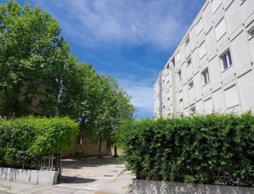 Hotel Mistral exterior view featuring green trees, a hedge, and the building facade under a blue sky.