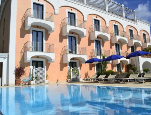 Hotel Murmann vista esterna con piscina, ombrelloni blu e balconi. Ideale per vacanze e relax. Servizi alberghieri di alta qualità.