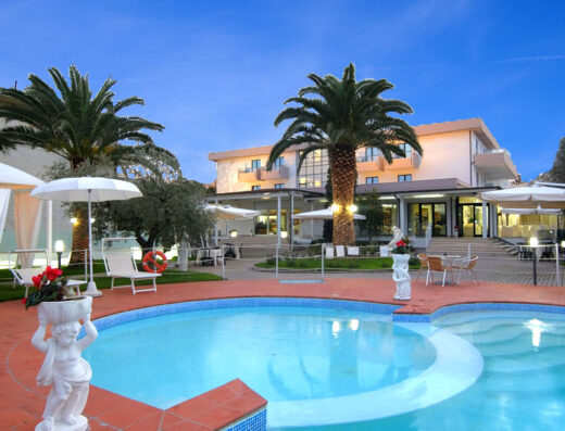 Hotel Parco degli Ulivi vista piscina esterna con palme, sedie a sdraio e gazebo per un relax estivo in un ambiente accogliente.