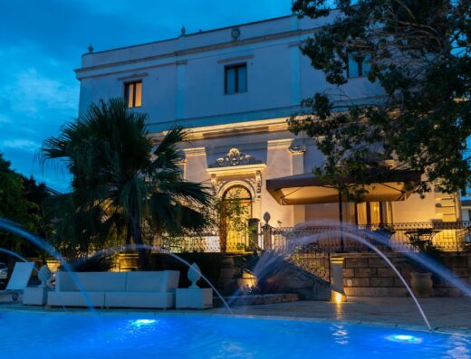 Hotel Parco Delle Fontane: vista notturna della facciata dell'hotel con piscina illuminata e fontane decorative in primo piano.
