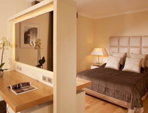 Interni di Hotel Piccolo Borgo: camera da letto con letto matrimoniale, comodini con lampade, scrivania con orchidea e rivista.