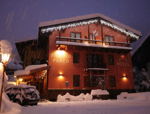 Hotel Piccolo Parco in inverno, con neve, illuminazione festiva e auto coperta di neve. Atmosfera accogliente per vacanze sulla neve.