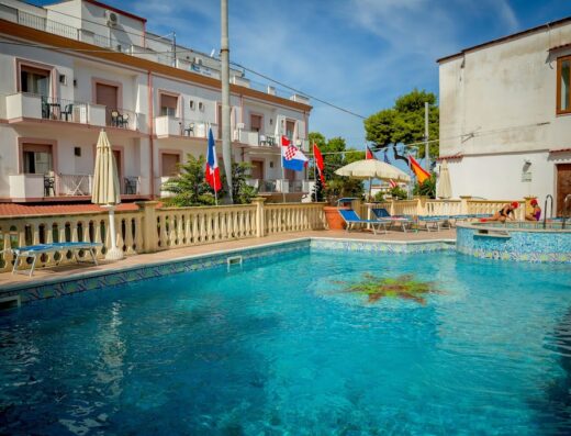 Hotel Pineta: ampia piscina con acqua cristallina, bandiere decorative e zona relax con lettini prendisole per un soggiorno indimenticabile.