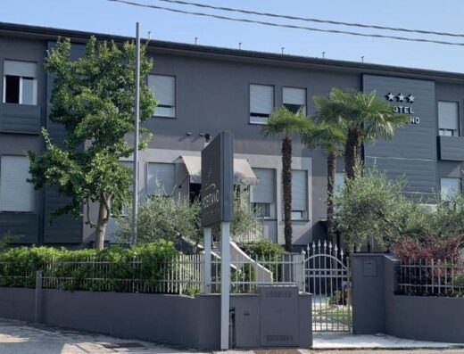 Hotel Positano: Facade of a modern hotel in Positano, Italy, with a three-star rating, palm trees, a sign, and a gated entrance.