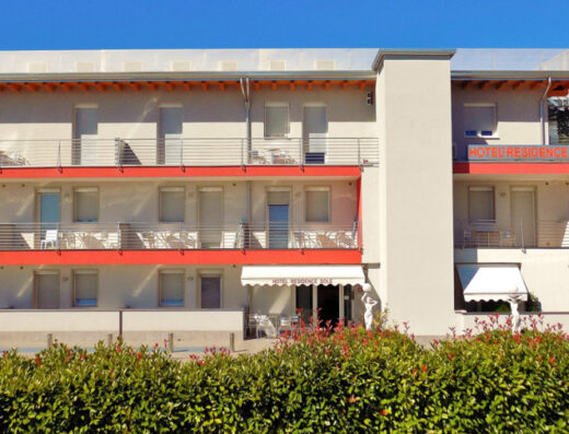 Hotel Residence Sole esterno, struttura a tre piani con balconi e arredi esterni, insegna visibile. Facciata bianca con dettagli arancioni, vegetazione in primo piano.