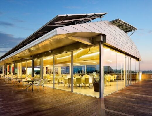 Hotel Ristorante I Castelli's elegant outdoor dining area with wooden flooring, glass walls, and a modern roof structure, offering a scenic view at sunset.