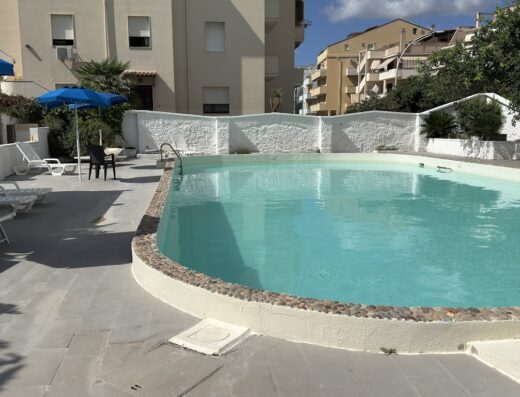 Piscina all'aperto dell'Hotel Riviera con acqua cristallina, circondata da lettini prendisole e ombrelloni blu, ideale per relax e vacanze estive.