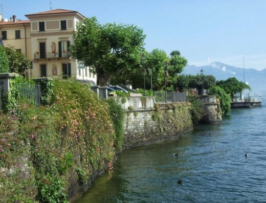 Hotel Riviera affacciato sul lago, con vegetazione rigogliosa e montagne sullo sfondo, offre un'esperienza di viaggio unica.