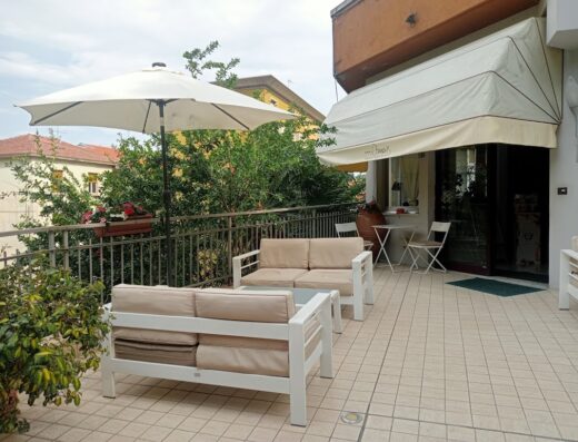 Terrazza esterna dell'Hotel Roma con divani bianchi da esterno, ombrellone e tavolino. Un'oasi di relax ideale per i viaggiatori.