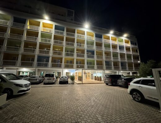 Hotel Roma Tor Vergata di notte, facciata illuminata con balconi colorati, parcheggio con auto, atmosfera accogliente e moderna.