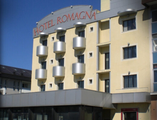 Hotel Romagna: Facciata dell'albergo con balconi cilindrici, insegna rossa "Hotel Romagna" e cielo blu sullo sfondo, ideale per viaggi e turismo.