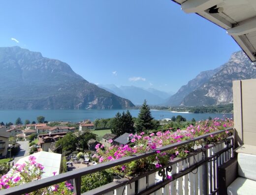 Vista panoramica sul lago di Ledro dall'Hotel Saligari, con montagne sullo sfondo e fiori colorati sul balcone.