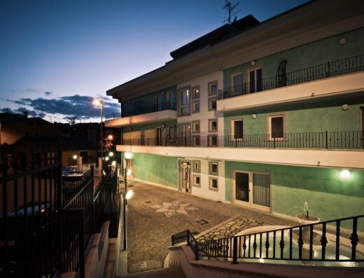 Hotel San Berardo: vista esterna notturna dell'hotel con illuminazione soffusa, balconi, vialetto decorato e fontana, ideale per un soggiorno rilassante.