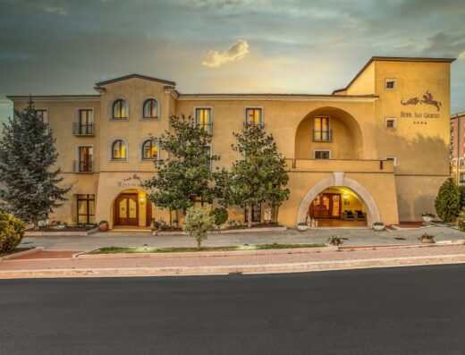 Hotel San Giorgio in Italy with a yellow facade, arched entrance, trees, and clear sky