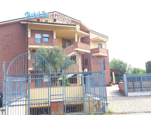 L'Hotel San Giorgio, una struttura in mattoni rossi con balconi, insegna blu e un cancello di metallo all'ingresso, offre un'accogliente ospitalità per viaggiatori e motociclisti.