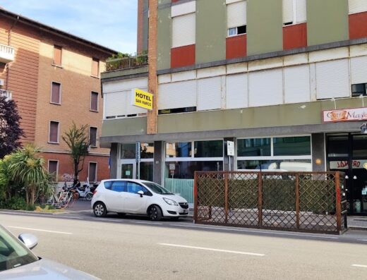 Hotel San Marco a Forlì, Italia. Vista esterna dell'hotel con insegna gialla "Hotel San Marco", auto parcheggiata e moto sullo sfondo. Servizi alberghieri e accoglienza viaggiatori.