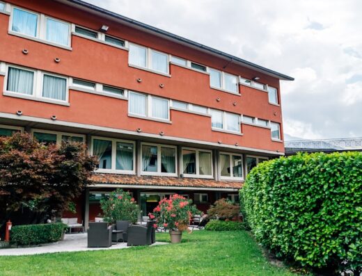 Esterno dell'Hotel San Martino con giardino curato, area relax con divanetti e vista sulla struttura color terracotta.