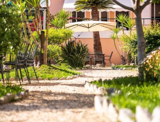 Hotel San Michele Celle: Vista del giardino con tavolo e sedie sotto l'ombrellone, vialetto di ghiaia e vegetazione lussureggiante.
