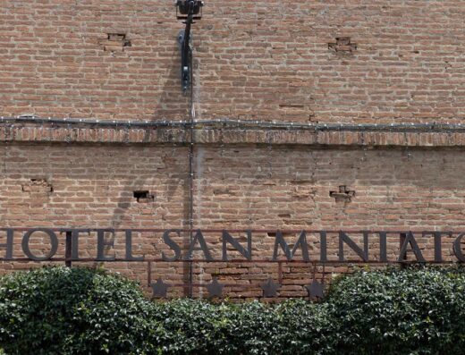 Hotel San Miniato sign on a brick wall partially obscured by green bushes.