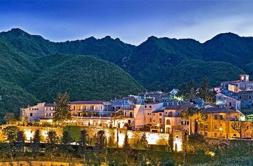 Veduta panoramica notturna dell'Hotel Scapolatiello, immerso nel suggestivo paesaggio montano circostante. Edifici illuminati creano un'atmosfera accogliente.