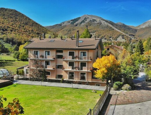 Hotel Sport Daniel vista esterna con prato verde, piscina coperta e sullo sfondo le montagne dell'Appennino abruzzese.