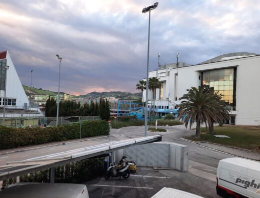 Vista esterna dell'Hotel Sporting con una moto parcheggiata sotto un porticato, illuminazione stradale e architettura moderna sullo sfondo.