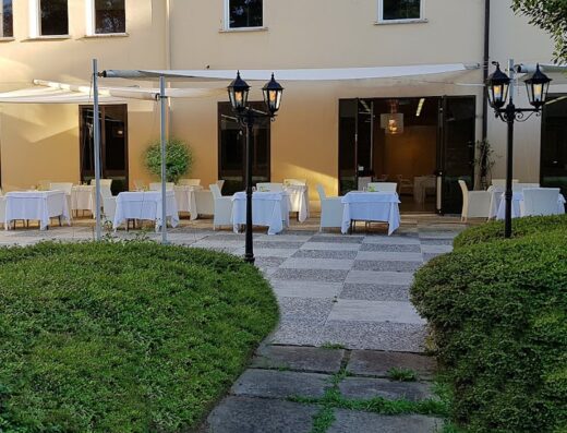 Veranda esterna del Hotel Terme di Castel San Pietro con tavoli apparecchiati e vegetazione curata. Ristorante all'aperto per eventi e relax.