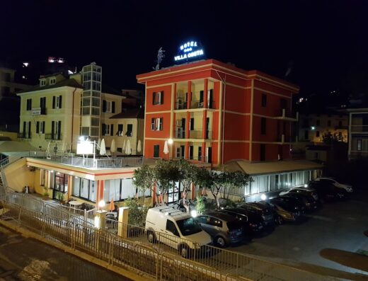 Hotel Villa Costa di Ciuffo at night, featuring the building's exterior, parked cars, and illuminated signage, showcasing its architecture and location.