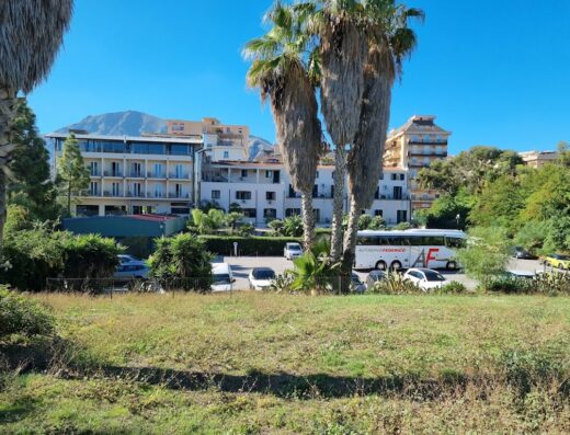 Hotel Villa D'Amato: vista esterna dell'hotel con parcheggio, autobus e vegetazione circostante in una giornata di sole a Palermo.