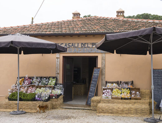 I Casali del Pino store front featuring fresh, locally grown organic produce displayed on hay bales under black umbrellas.