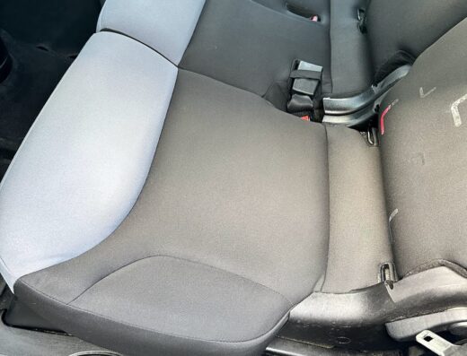 Sedile posteriore di un'auto con rivestimento bicolore grigio e nero, cinture di sicurezza visibili e dettaglio della chiave dell'auto in primo piano.