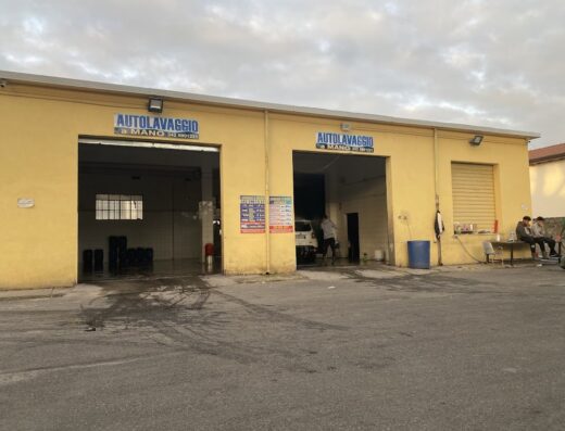 I Faraoni Autolavaggio a Mano: Facciata esterna gialla con due ingressi per il lavaggio auto. Persone sedute fuori.